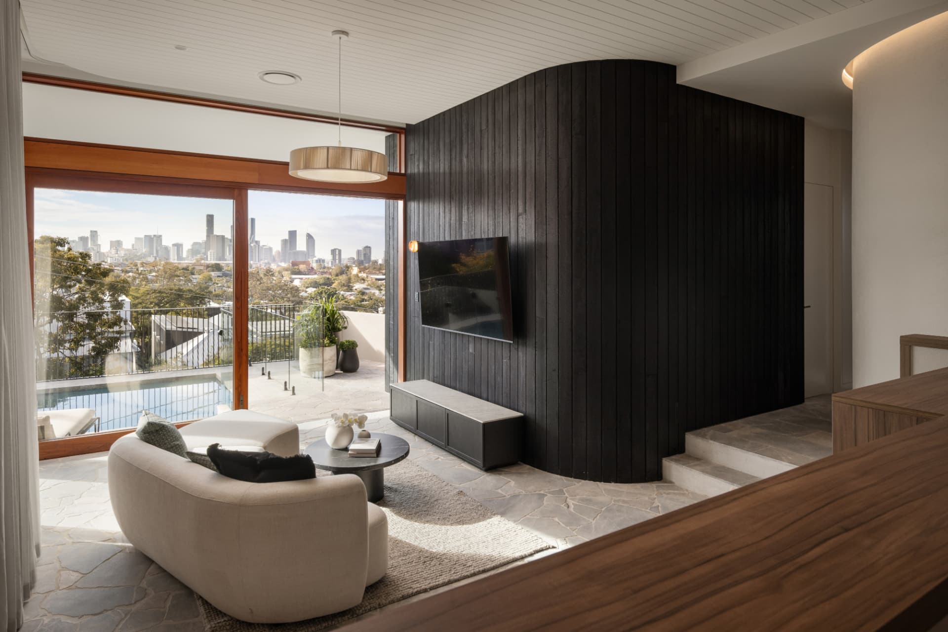 Poolside living pavilion with curved black timber wall and city views